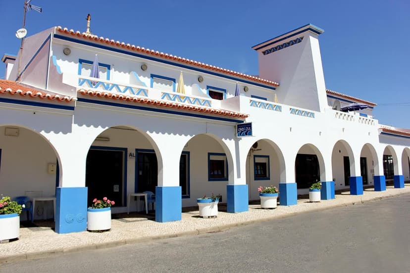 White building with blue trim, arched portico, and potted flowers under a clear blue sky.