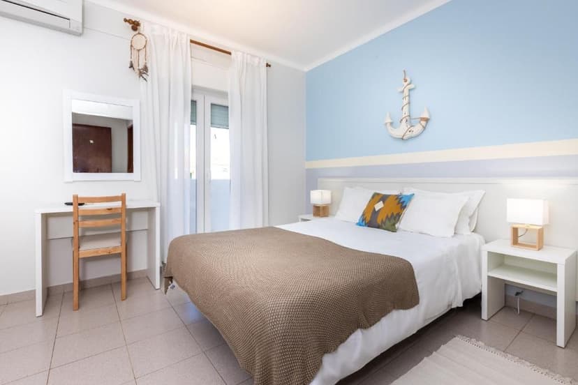 Bedroom with white bedding, brown throw, and nautical anchor decor on blue wall