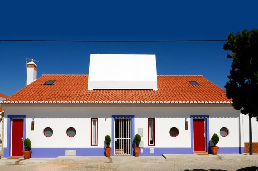White house with orange tiled roof, blue trim, and red doors under a clear blue sky.