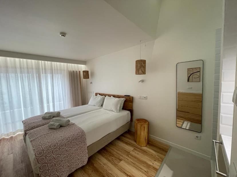 Twin beds with white linens, patterned throw, and wooden accents in a bright hotel room.