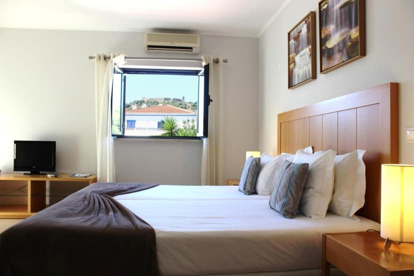 Hotel bedroom with twin beds, view of white building and distant hill fort through open window.