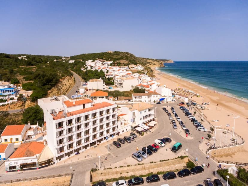 Coastal town with white buildings, hotel, and parking lot next to a wide sandy beach and blue ocean.