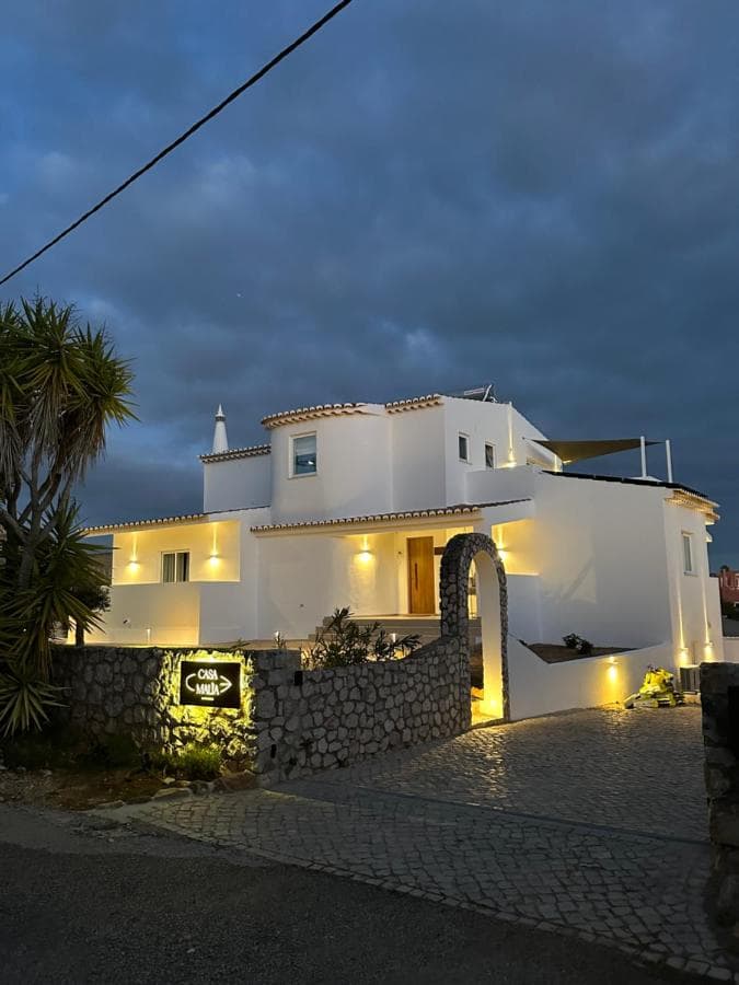 White modern villa illuminated at dusk with stone wall entrance and "Casa Malua" sign