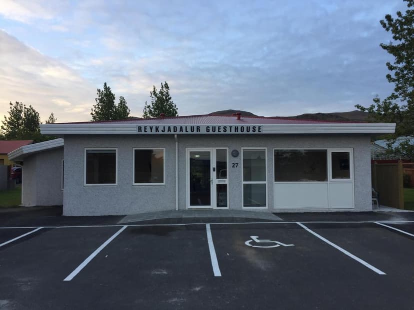 Reykjadalur Guesthouse entrance with accessible parking space and mountains in background.