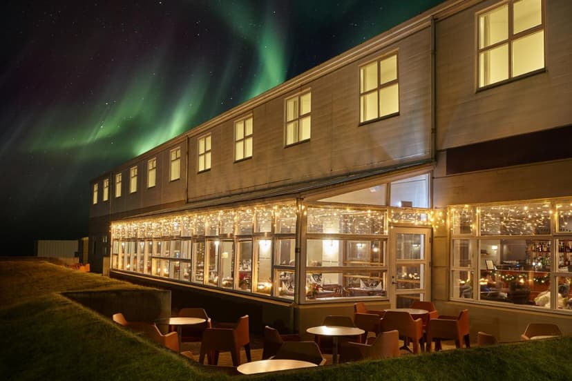 Hotel building exterior at night with Northern Lights visible over the illuminated glass dining area.
