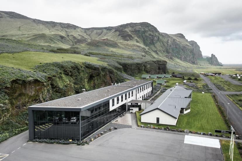 Hotel VíK í Mýrdal complex nestled against steep, green Icelandic mountains under an overcast sky.