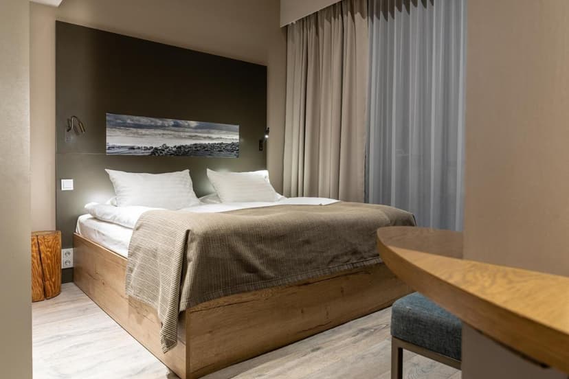 Hotel room in Vík í Mýrdal with wooden bed, white linens, and coastal artwork.
