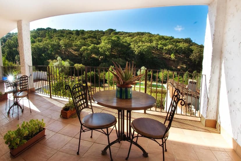 Balcony with wrought iron furniture overlooking a dense green hillside under a blue sky at Hotel Posada San Marcos.