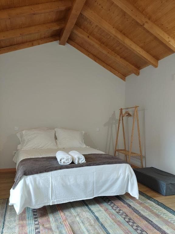 Bedroom with white linens, wooden beamed ceiling, and colorful patterned rug