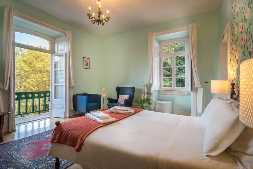 Bedroom with white linens, blue chairs, and balcony view of yellow autumn trees