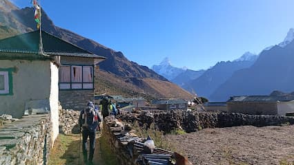 Hikers walking past stone buildings toward snow-capped mountains near Pheriche.