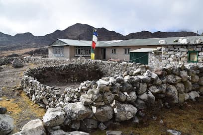 Tashi Delek Lodge Thagnak with stone walls and prayer flags against barren mountains.