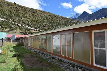 Machhermo Lodge & Bakery with long row of windows against grassy mountain slope and peaks.