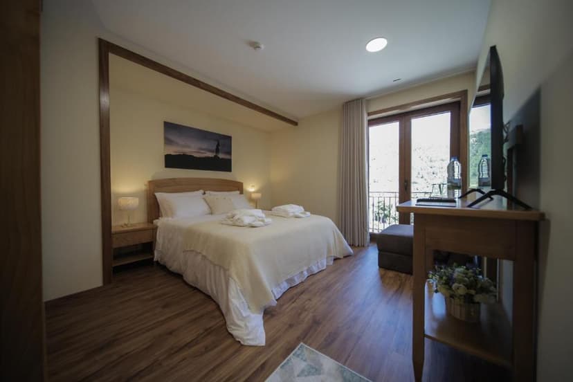 Bedroom with wooden floors, double bed, and balcony view of green hills, Casa da Fonte.