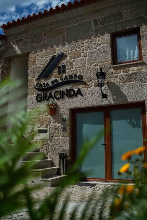 Stone building entrance with "Casa do Campo Gracinda" sign, seen through foreground foliage.