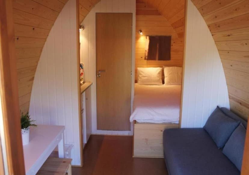 Interior of a wooden pod or cabin showing a bed, sofa, and small table in Parque Biologico de Vinhais.