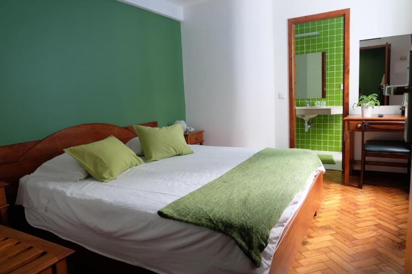 Hotel Alcides bedroom with wooden bed, green accent wall, and bright green tiled bathroom visible.