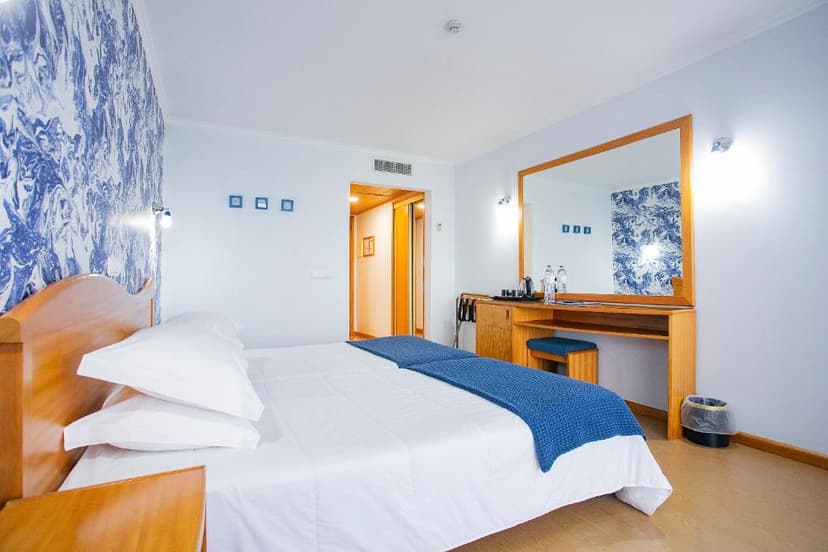 Hotel room with white bedding, blue accents, wooden furniture, and a large mirror.