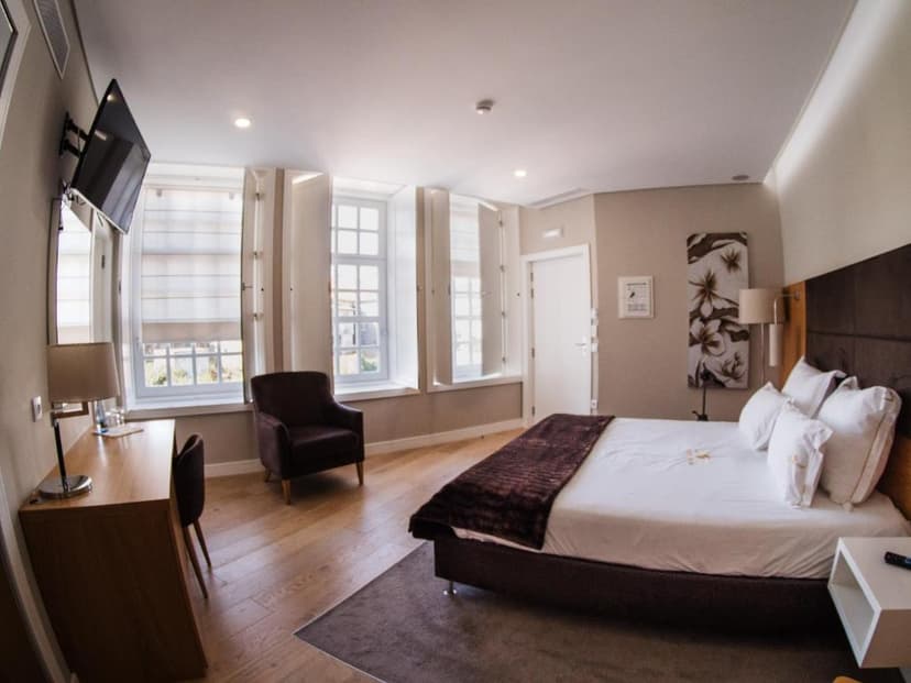 Hotel room interior with large bed, wooden desk, armchair, and windows with white shutters