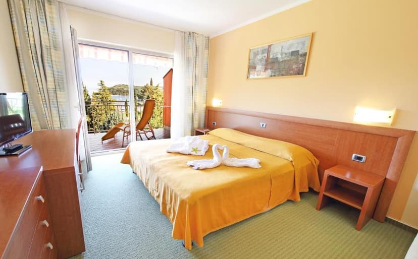 Hotel room with yellow bedspread, towel swans, and balcony view of trees and water.
