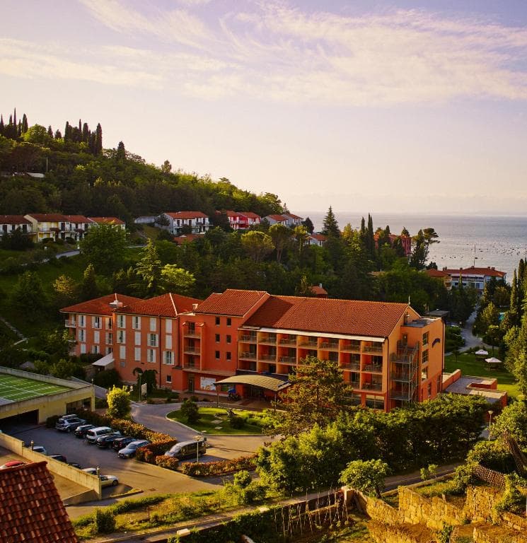 Orange resort building with terracotta roof nestled in green hillside near the sea.