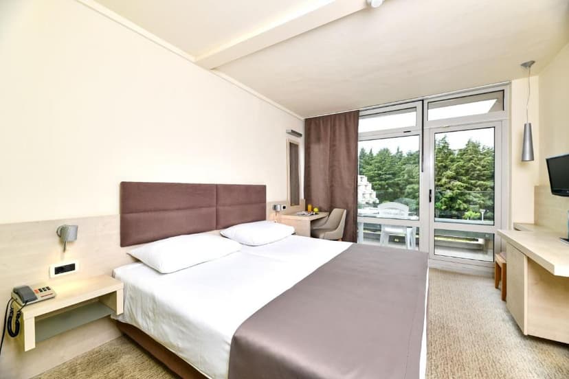 Hotel room with double bed, balcony access, and view of green trees in Hotel Mediteran Plava Laguna.
