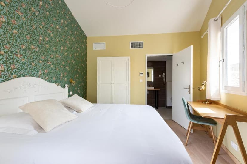 Hotel room with white bedding, green patterned wallpaper, and an open doorway to a dark bathroom.