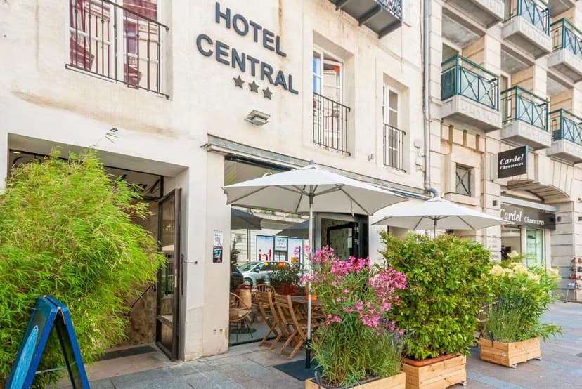 Hotel Central entrance with outdoor seating, white umbrellas, and potted flowering plants.