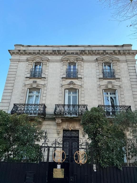 Stone mansion with ornate balconies and black wrought iron gate in Arles.