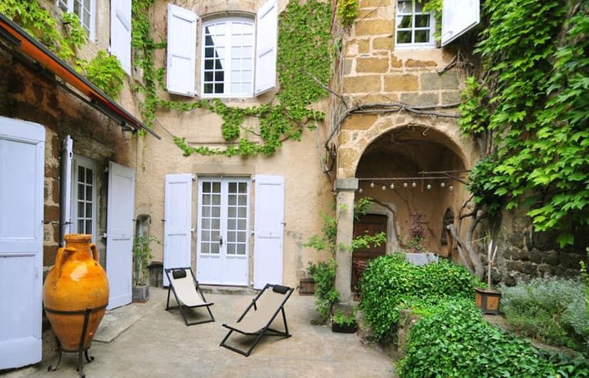 Courtyard with stone walls, white shutters, and lush green ivy, likely in La Demeure du Lac de Fougères.