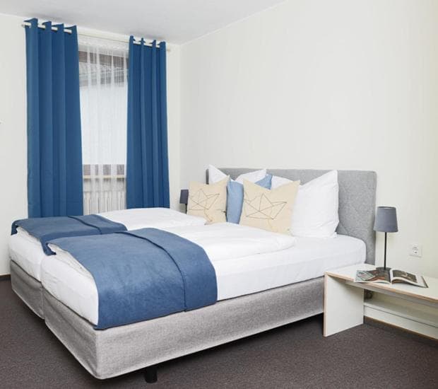 Twin beds with white linens and blue throws in a bright room with blue curtains at Senefelder Hof.