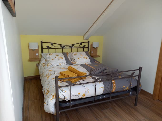 Double bed with yellow and grey floral bedding in attic room in Les Hauts du Cheylard