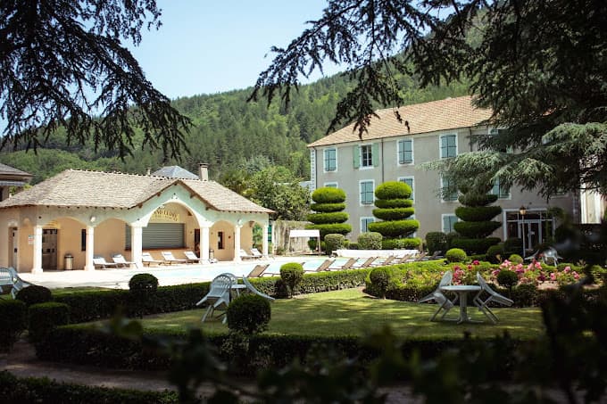 Grand Hôtel du Parc hotel exterior with pool, manicured gardens, and forested mountain backdrop.