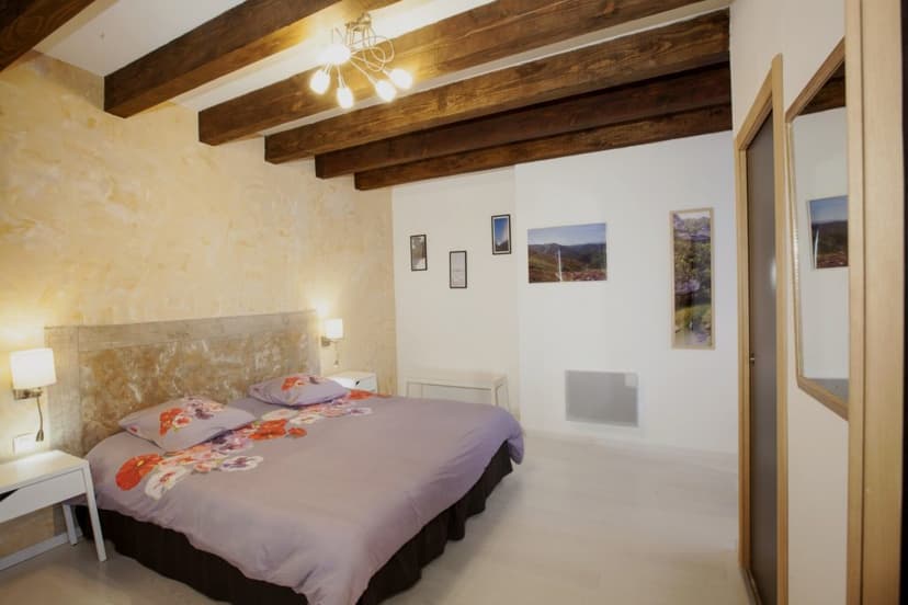 Bedroom with exposed wooden beams, lavender floral duvet, and textured yellow accent wall