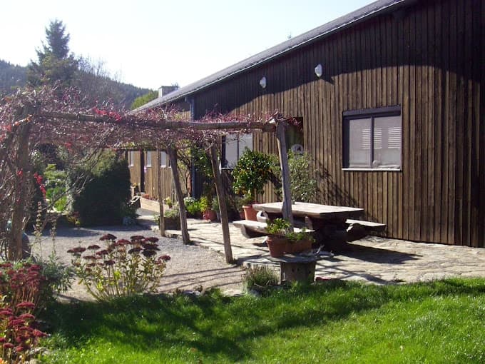 Wooden building exterior with pergola, picnic table, and garden in a hilly setting.