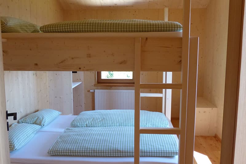 Bunk beds with green gingham bedding inside a wood-paneled room at Falkenstein Schutzhaus.