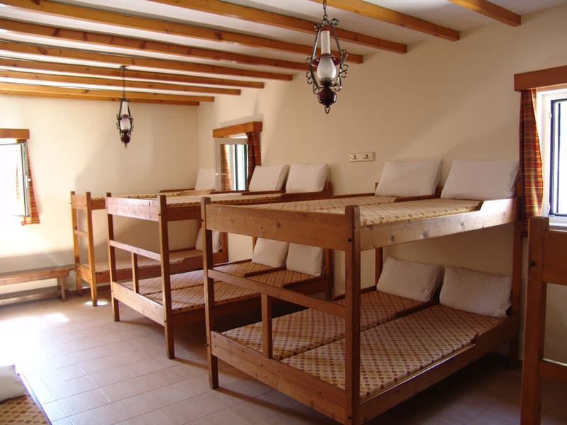 Dormitory room with wooden bunk beds, white pillows, and exposed ceiling beams at Spilios Agapitos Refuge.
