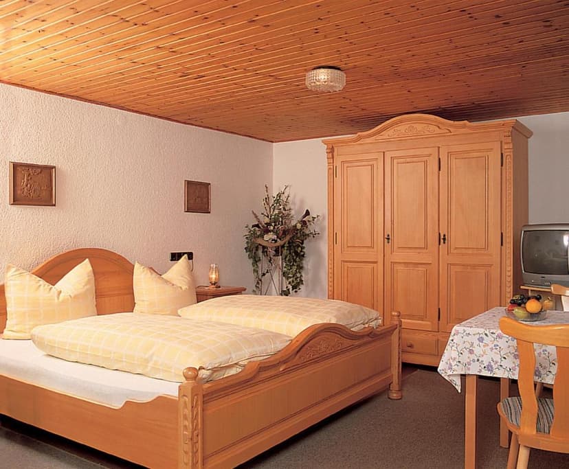 Guest room in Gasthaus-Pension Weber with wooden bed, wardrobe, and small dining table.