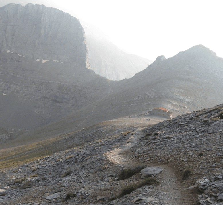 Hiking trail leading to a refuge building nestled between steep, rocky mountainsides.