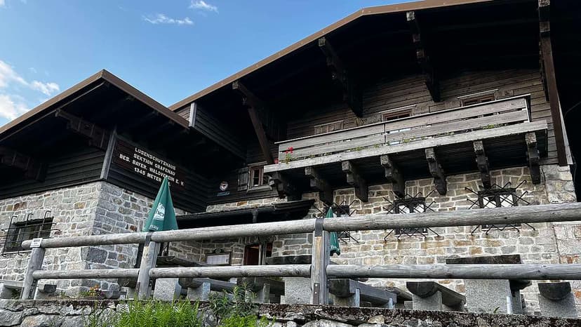 Lusen-Schutzhaus built of stone and dark wood with a wooden fence railing in foreground.