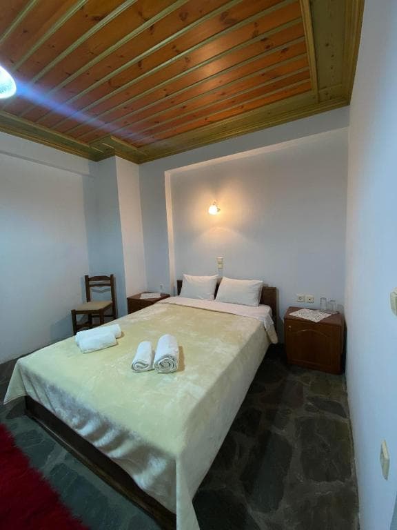 Hotel room with wooden plank ceiling, stone floor, and double bed with white towels in Zagori.