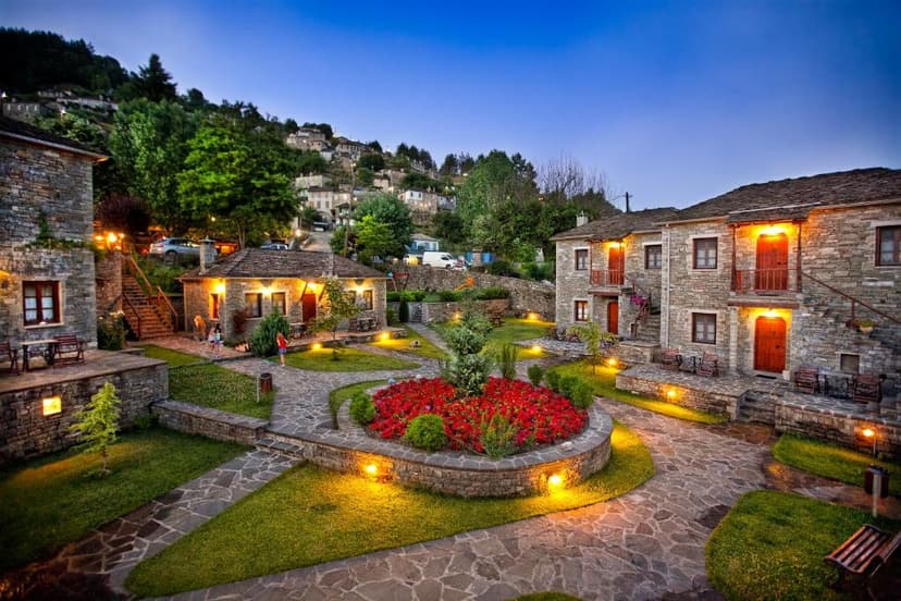 Stone hotel complex courtyard with flower bed and illuminated pathways at dusk in a hillside village.