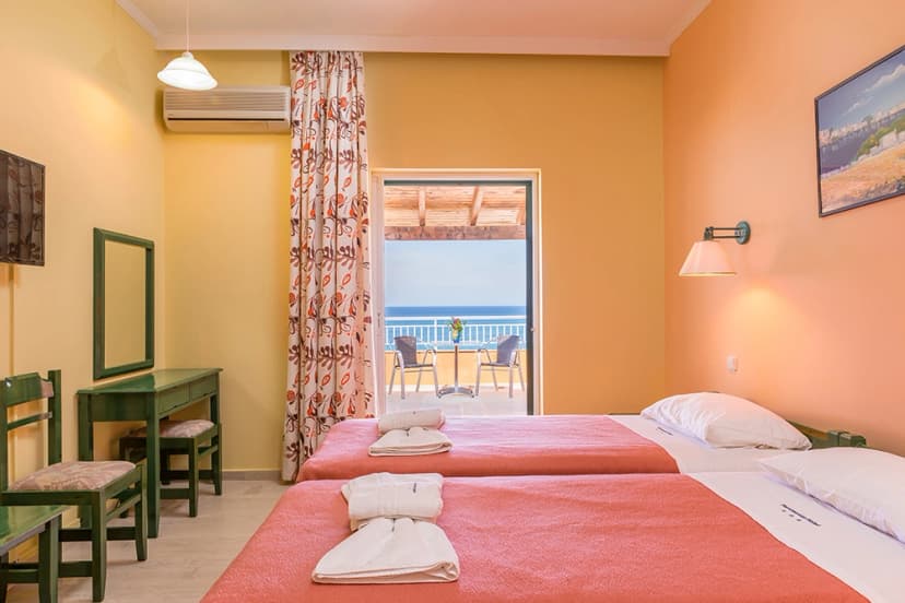 Twin hotel room with beds, green furniture, and balcony view of the sea.
