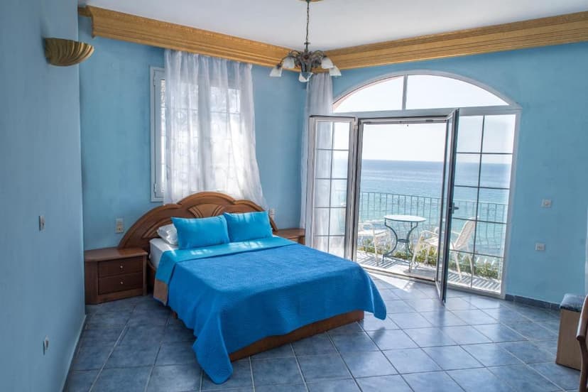 Bedroom with blue decor, wooden bed, and balcony overlooking the sea.