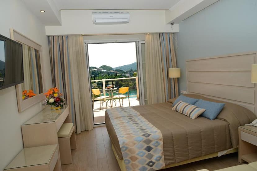 Hotel room with double bed, balcony view of green hills and coastal buildings