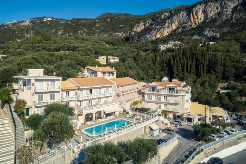 Pink hotel complex with swimming pool nestled against steep, forested mountainside