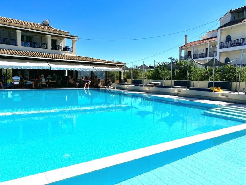 Bright blue swimming pool next to hotel buildings with outdoor dining area.
