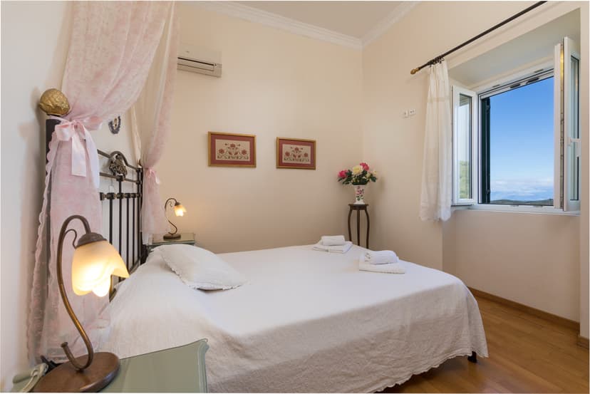 Bedroom with white linens, pink canopy, and sea view from open window in Corfu.