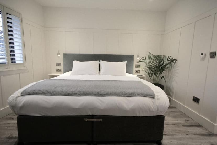 Boutique townhouse bedroom with white paneled walls, grey headboard, and large potted plant.