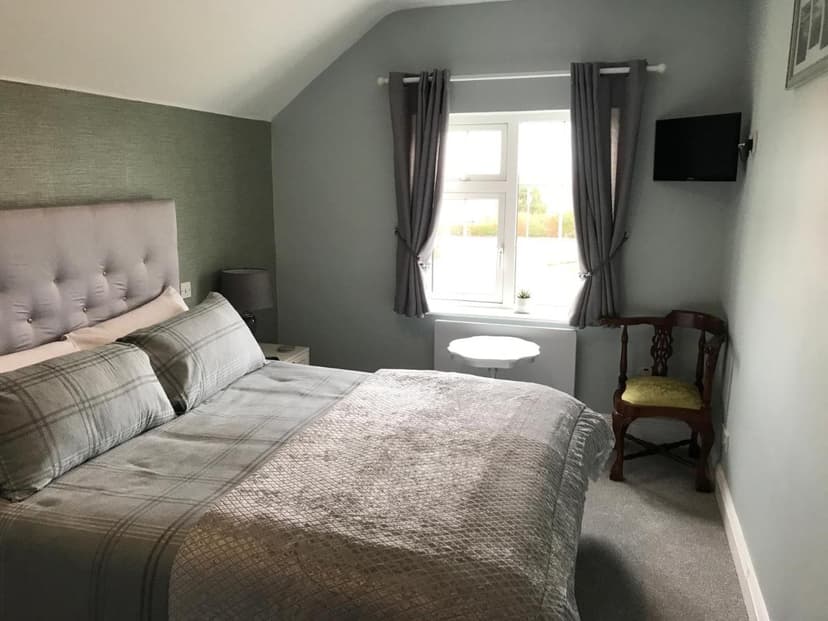 Bedroom at Kielty's of Kerry with grey plaid bedding, tufted headboard, and window.